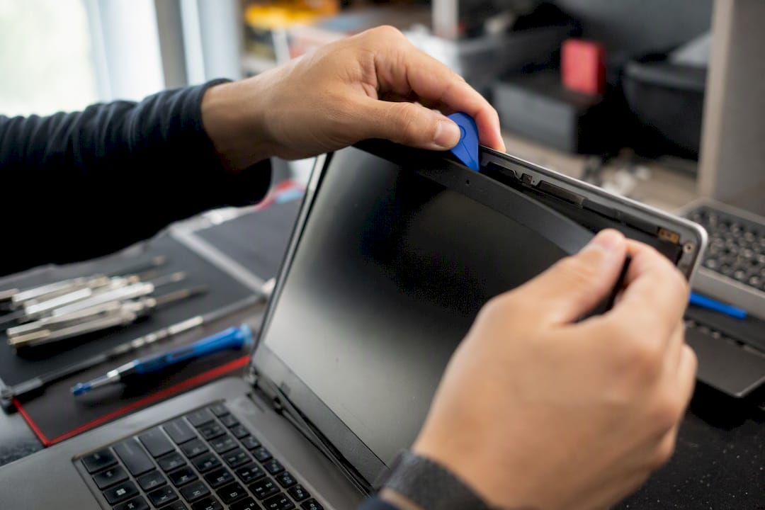 Des mains retirant le contour de l'écran d'un ordinateur portable avec un outil en plastique